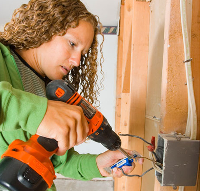 A woman using a drill to put together an electric outlet